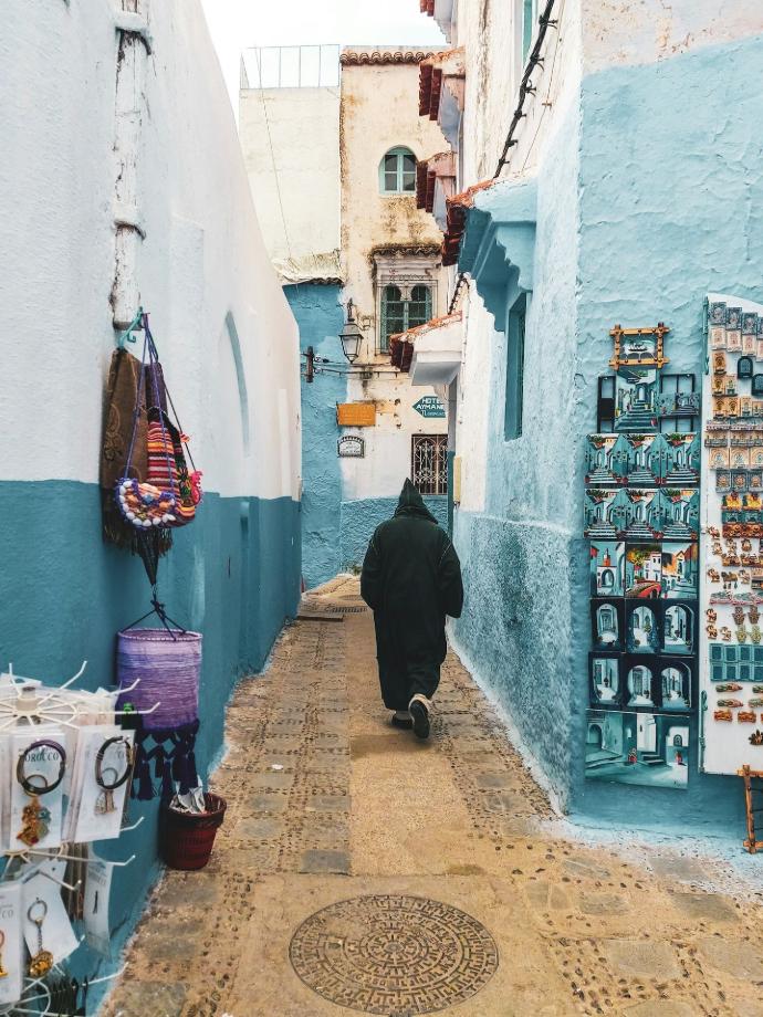 person wearing hooded jacket walking on alley between buildings during daytime